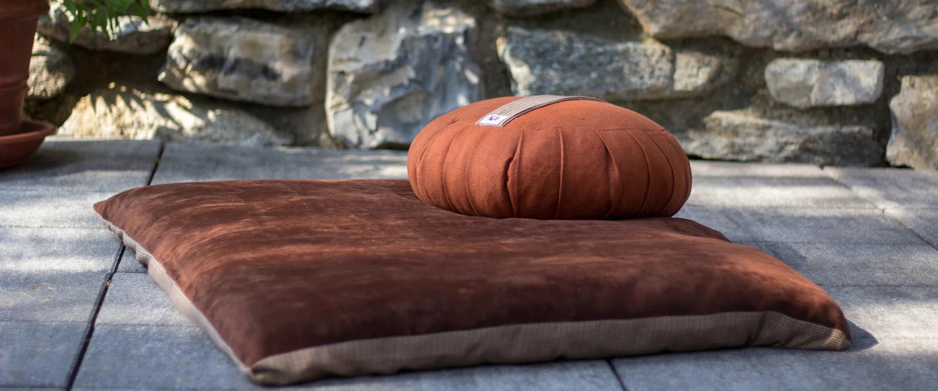 An orange zafu on top of a zabuton with a stony background.